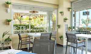 Modernisti sisustettu kahvila, jossa on pöytiä ja tuoleja; näkymä vehreisiin puihin ja ulkokalusteisiin. (Tekoälyn luoma teksti)