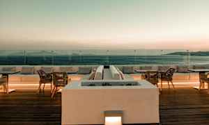 Terassi, jolla on istumapaikkoja ja pöytiä näkymällä merelle auringonlaskun aikaan. (Tekoälyn luoma teksti)