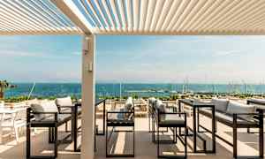 Ulkoterassi, josta on näkymä merelle, sohvia ja pöytiä pergolan alla. (Tekoälyn luoma teksti)