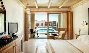 Hotellihuone puuyksityiskohdilla, mukaan lukien suuri sänky ja istuma-alue, sekä parvekkeen ovi, joka johtaa altaalle. (Tekoälyn luoma teksti)