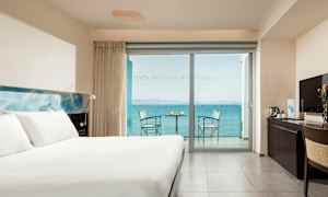 Hotellihuone, jossa on iso sänky, työpöytä ja parveke merinäköalalla. (Tekoälyn luoma teksti)