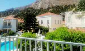 Kuvassa näkyy ulkoalue, jossa on uima-allas, rakennuksia ja vuoristoinen tausta. (Tekoälyn luoma teksti)