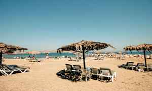 Ranta, jossa aurinkotuoleja ja olkikattoisia aurinkovarjoja. (Tekoälyn luoma teksti)