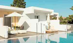 Valkoinen rakennus, jossa on ulkoterassi ja aurinkotuoleja uima-altaan äärellä. (Tekoälyn luoma teksti)