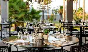 Ulkoilmaravintola, jossa pöydät on katettu laseilla ja aterimilla. (Tekoälyn luoma teksti)