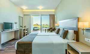 Kuva hotellihuoneesta, jossa on kaksi erillistä sänkyä, moderni sisustus ja suuret ikkunat näkymällä terassille. (Tekoälyn luoma teksti)