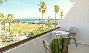 Parveke, jossa pöytä, tuolit ja näkymä vehreään puutarhaan palmuineen sekä mereen taustalla. (Tekoälyn luoma teksti)