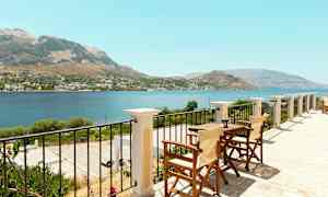 Näkymä terassilta, jossa on pöytiä ja tuoleja, meri ja vuoret näkyvät. (Tekoälyn luoma teksti)