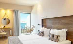 Hotellihuone, jossa on moderni sisustus, parisänky, työpöytä ja näkymä merelle parvekkeelta. (Tekoälyn luoma teksti)