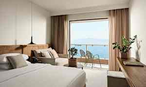 Hotellihuone, jossa on sänky, sohva ja näkymä merelle parvekkeelta. (Tekoälyn luoma teksti)