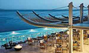 Ravintola puisilla tuoleilla ja pöydillä altaan vieressä, meri taustalla. (Tekoälyn luoma teksti)