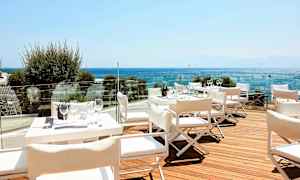 Terassi, jolla on valkoisia pöytiä ja tuoleja, näkymä merelle. (Tekoälyn luoma teksti)