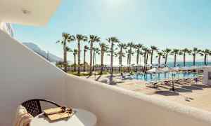 Näkymä parvekkeelta uima-altaalle, aurinkotuoleja ja palmuja auringonpaisteessa. (Tekoälyn luoma teksti)