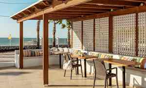 Ulkoterassi, jossa on puisia kalusteita, värikkäitä tyynyjä ja merinäköala. (Tekoälyn luoma teksti)