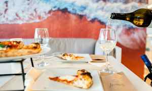 Pöytä, jossa pizzaa ja viinilaseja; taustalla kuva rannasta. (Tekoälyn luoma teksti)