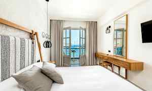 Valoisa ja modernisti sisustettu hotellihuone, jossa on sänky ja näkymä merelle parvekkeelta. (Tekoälyn luoma teksti)