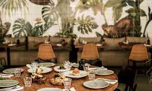 Katettu puupöytä, jota ympäröivät tuolit, taustalla seinämaalauksia kasviaiheilla. (Tekoälyn luoma teksti)