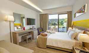 Hotellihuone, jossa on sänky, työpöytä, televisio ja parveke vihreällä näkymällä. (Tekoälyn luoma teksti)