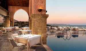 Ulkoilmaravintola katettuine pöytineen uima-altaan äärellä, merinäkymä auringonlaskussa. (Tekoälyn luoma teksti)