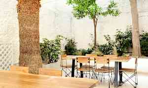 Ulkoruokapöytä ja puutuolit, ympäröitynä vihreillä kasveilla ja valkoisilla seinillä. (Tekoälyn luoma teksti)