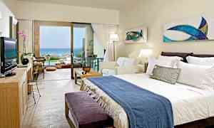 Hotellihuone, jossa on parivuode, sohva ja suuri lasiovi, joka johtaa terassille merinäköalalla. (Tekoälyn luoma teksti)