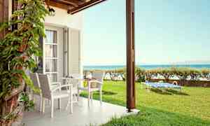 Terassi, jossa pöytä ja tuolit sekä aurinkotuoleja nurmikolla lähellä merta. (Tekoälyn luoma teksti)