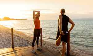 Kaksi henkilöä venyttelee puisella laiturilla rannalla auringonlaskun aikaan. (Tekoälyn luoma teksti)