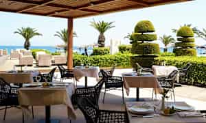 Ulkoterassi katetuilla pöydillä, palmuja ja näkymä merelle. (Tekoälyn luoma teksti)