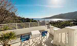 Näkymä terassilta pöydän ja tuolien kera, taustalla meri ja vuoret. (Tekoälyn luoma teksti)