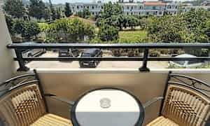 Parveke, jossa kaksi tuolia ja pyöreä pöytä tuhka-astialla, näkymä pysäköintialueelle ja vihreään ympäristöön. (Tekoälyn luoma teksti)