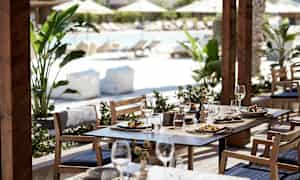 Ulkokalusteet, joille on laitettu ruokaa ja juomaa, taustalla allasalue. (Tekoälyn luoma teksti)