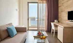 Huone, jossa on beige sohva, pöytä hedelmien ja mehun kera ja parvekeovi näkymällä. (Tekoälyn luoma teksti)