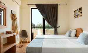 Huone, jossa on kaksi yhden hengen vuodetta, suuri ikkuna tummilla verhoilla ja parvekekalusteet ulkopuolella. (Tekoälyn luoma teksti)