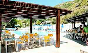 Ulkouima-allasalue, jossa on aurinkotuoleja, aurinkovarjoja, pöytiä ja tuoleja varjostavan katon alla. (Tekoälyn luoma teksti)