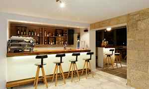 Moderni baaritiski, jossa on korkeat tuolit, hyllyillä pulloja ja kirkas valaistus. (Tekoälyn luoma teksti)