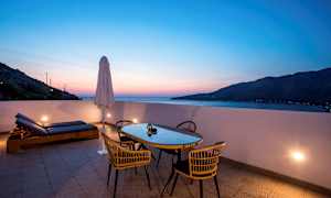 Terassi pöydän, tuolien ja aurinkotuolien kanssa auringonlaskun aikaan. (Tekoälyn luoma teksti)