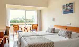 Hotellihuone, jossa on kaksi yhden hengen vuodetta, istuinryhmä ja näkymä vehreään ympäristöön. (Tekoälyn luoma teksti)