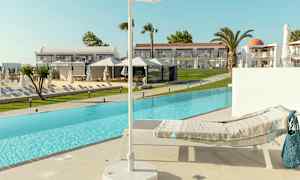 Aurinkotuoli, jossa on peitto uima-altaan reunalla, varjo etualalla ja hotellirakennukset taustalla. (Tekoälyn luoma teksti)