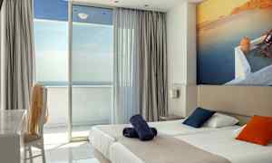 Hotellihuone, jossa on parivuode, värikkäät tyynyt ja parveke merinäköalalla. (Tekoälyn luoma teksti)