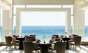 Nykyaikainen ravintola, josta on näkymä merelle, sisustettuna pyöreillä pöydillä ja mukavilla tuoleilla. (Tekoälyn luoma teksti)