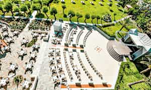 Ilmakuva ulkoterassista ja viheralueesta, jossa on puita ja aurinkovarjoja. (Tekoälyn luoma teksti)