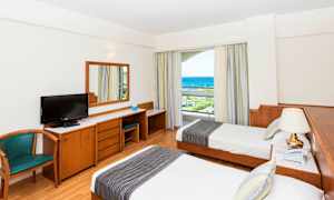 Hotellihuone, jossa kaksi erillistä vuodetta, työpöytä, tuoli ja merinäköala. (Tekoälyn luoma teksti)