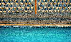 Ilmakuva rannasta, jossa on aurinkovarjoja ja aurinkotuoleja, ja merta etualalla. (Tekoälyn luoma teksti)