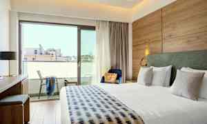 Hotellihuone, jossa on iso sänky, kirjoituspöytä, tuoli ja parveke. (Tekoälyn luoma teksti)