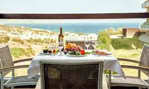 Pöytä liinalla, laseilla ja viinipullolla, ympärillä tuoleja, näkymä maisemaan ja merelle. (Tekoälyn luoma teksti)