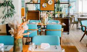 Modernisti sisustettu ravintolatilat, jossa pöytiä, turkooseja tuoleja ja koristekasveja. (Tekoälyn luoma teksti)