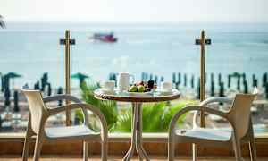 Kaksi tuolia pöydän ääressä, jossa hedelmiä ja juomaa, näkymä merelle. (Tekoälyn luoma teksti)