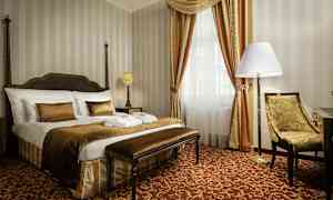 Tyylikäs hotellihuone, jossa on suuri sänky, tuoli ja verhoilla varustettu ikkuna. (Tekoälyn luoma teksti)