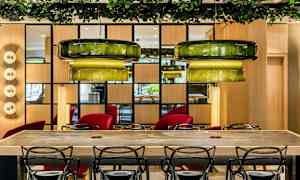 Nykyaikaisesti sisustettu huone, jossa tuoleja puupöydän ympärillä ja vihreät kattovalaisimet yläpuolella. (Tekoälyn luoma teksti)