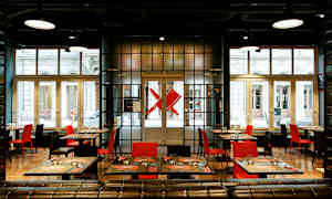 Moderni ravintola, jossa punaisia ja mustia tuoleja sekä katettuja pöytiä suurten ikkunoiden edessä. (Tekoälyn luoma teksti)